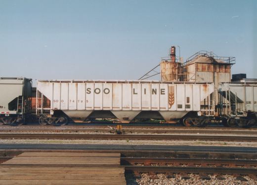 A white SOO Line freight car with number 74795 is parked on tracks next to a grain elevator on a sunny day.