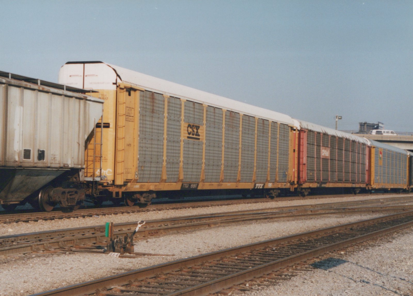 A side view of a train composed of yellow and red autoracks with CSX and GATX lettering, on a multi-track railroad line under a clear sky.