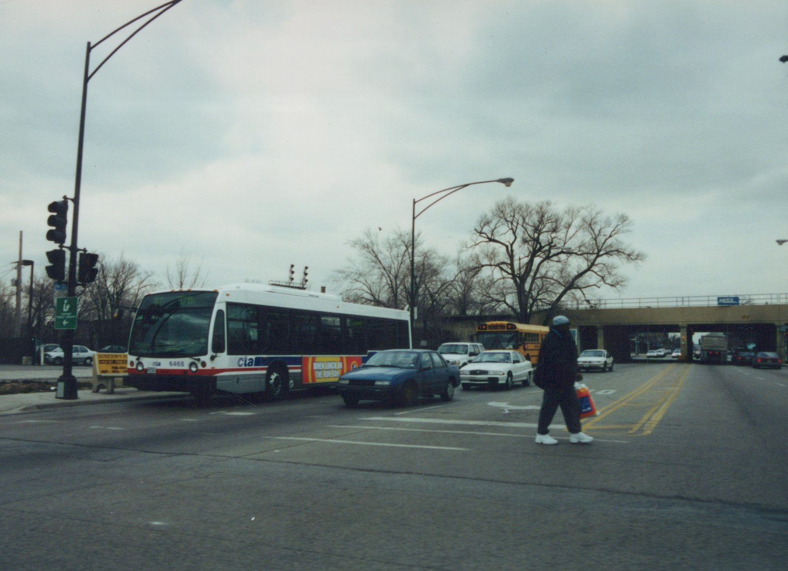A white and blue CTA bus numbered 6468 on route 87 to 57th Street is stopped at a street intersection under an overcast sky, with a pedestrian crossing the street and other vehicles nearby.