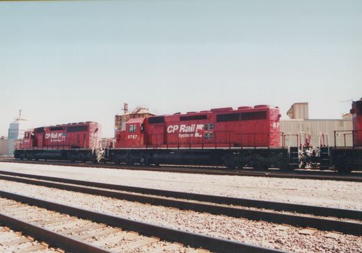 A side-view photograph of two red CP Rail System diesel locomotives, numbered 5757 and 5641, parked on parallel tracks in a gravel yard with industrial buildings in the background.
