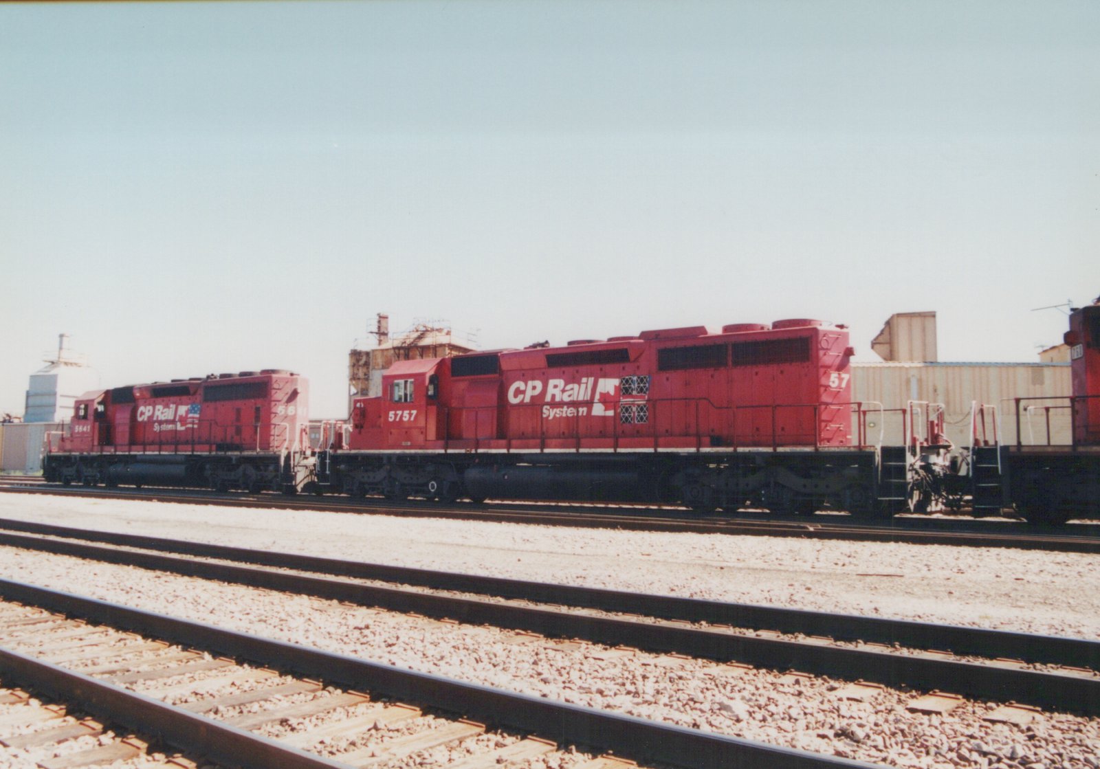 A side-view photograph of two red CP Rail System diesel locomotives, numbered 5757 and 5641, parked on parallel tracks in a gravel yard with industrial buildings in the background.
