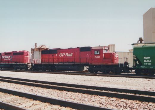A side view of two red Canadian Pacific GP9 locomotives, numbered 760 and 5757, coupled together on train tracks with a green AGPX freight car nearby, in a sunny yard setting.