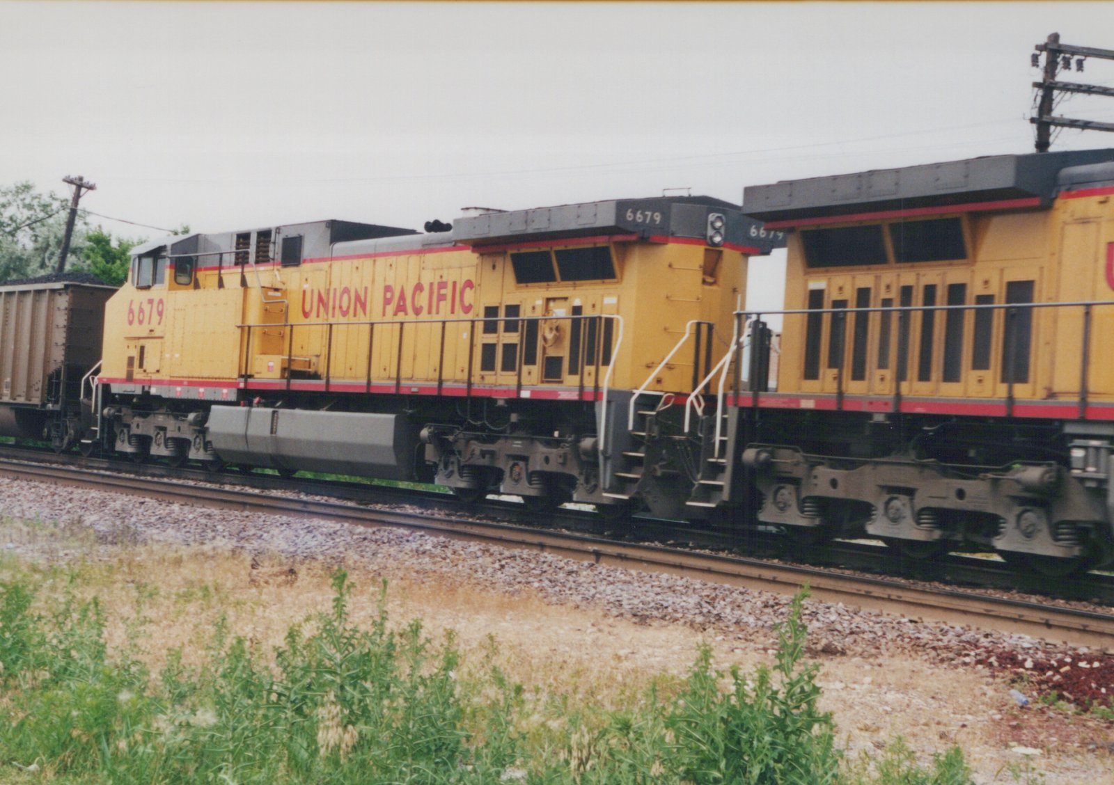 A yellow Union Pacific diesel locomotive with the number 6679 on its side is pulling a freight car along a set of tracks next to a grassy area.