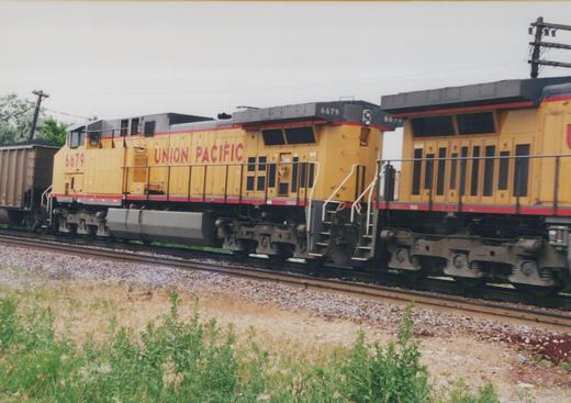 A yellow Union Pacific diesel locomotive with the number 6679 on its side is pulling a freight car along a set of tracks next to a grassy area.