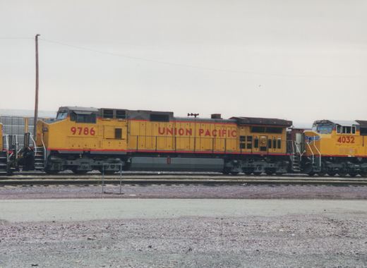 Side view of two yellow Union Pacific diesel locomotives, numbered 9786 and 4032, parked on parallel tracks in a gravel yard under a gray sky.