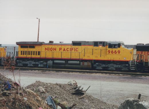A yellow and red Union Pacific diesel locomotive numbered 9669 is parked on tracks in an industrial yard under an overcast sky.