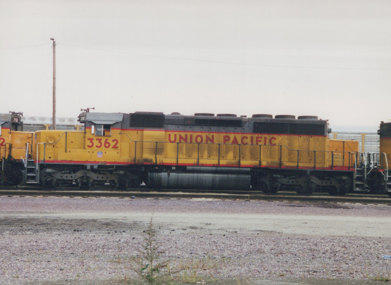 A side view of a Union Pacific diesel locomotive, number 3362, painted yellow with a gray roof and red stripe, parked on a railroad track in a gravel yard under an overcast sky.