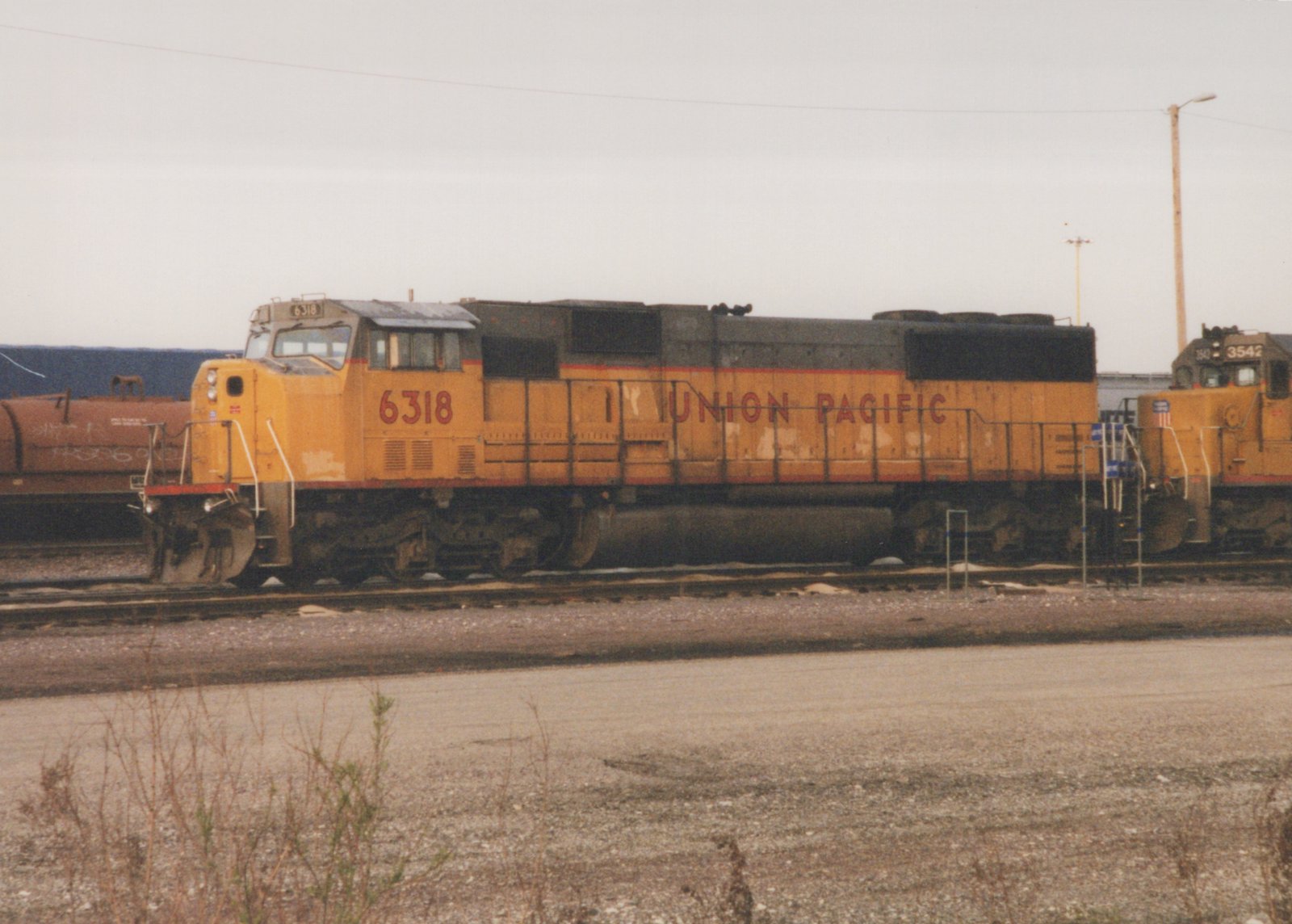 Side view of a yellow Union Pacific GP38-2 diesel locomotive, number 6318, in a railyard with another locomotive partially visible behind it under an overcast sky.