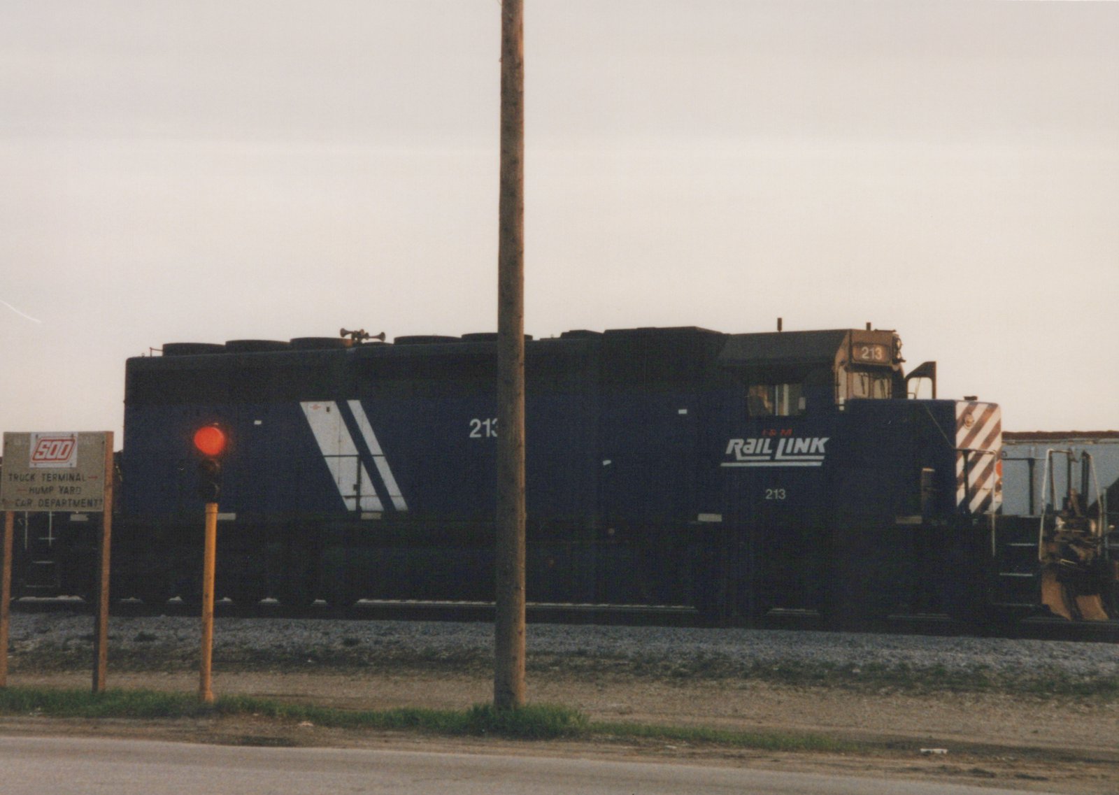 A dark blue I&M Rail Link diesel locomotive, numbered 213, sits in a rail yard; a sign for the Soo Line's truck terminal and hump yard is visible to the left.
