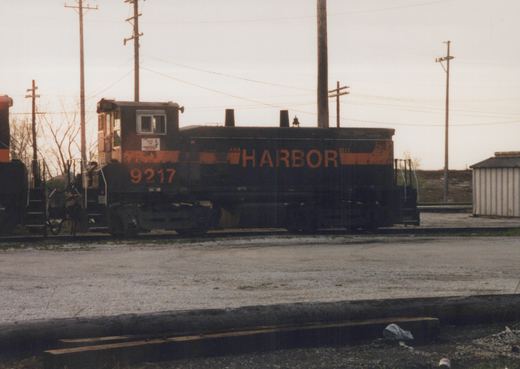 A black and orange Indiana Harbor Belt diesel locomotive, numbered 9217, stands on tracks in a gravel yard under an overcast sky.