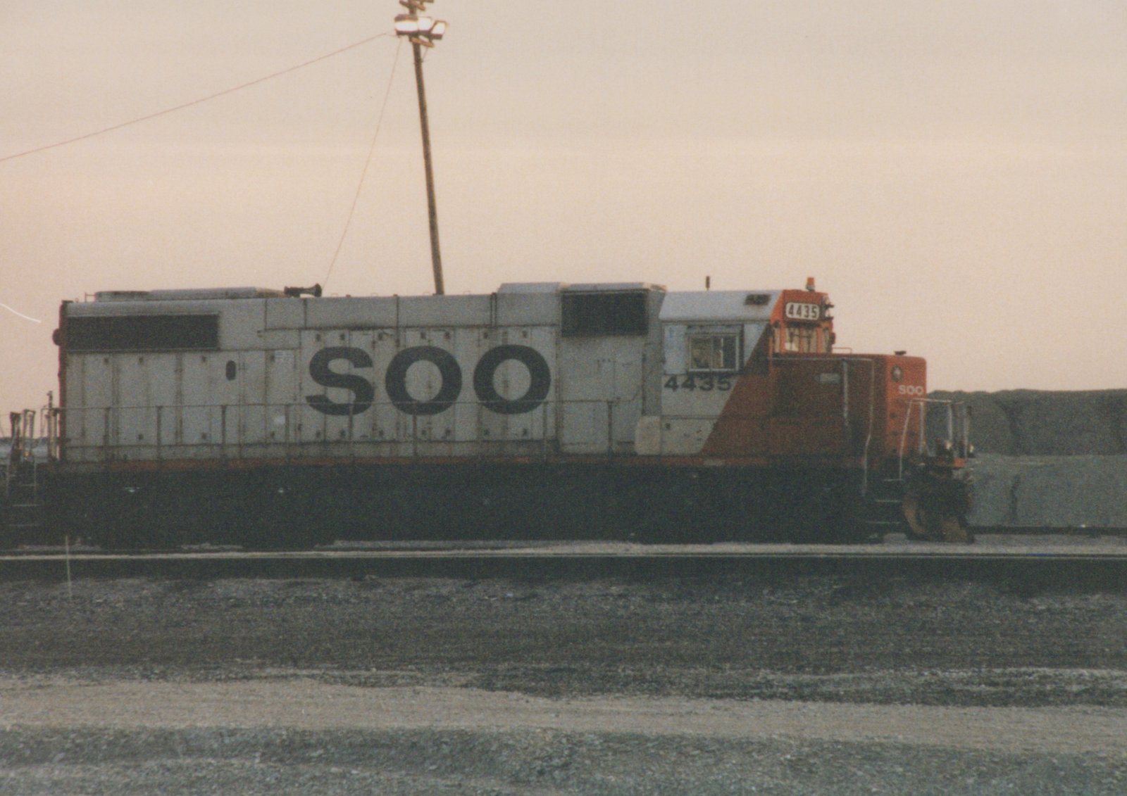 A side view of a SOO Line diesel locomotive, number 4435, in a rail yard at dusk. The locomotive is painted white with orange on the front and black underframe.