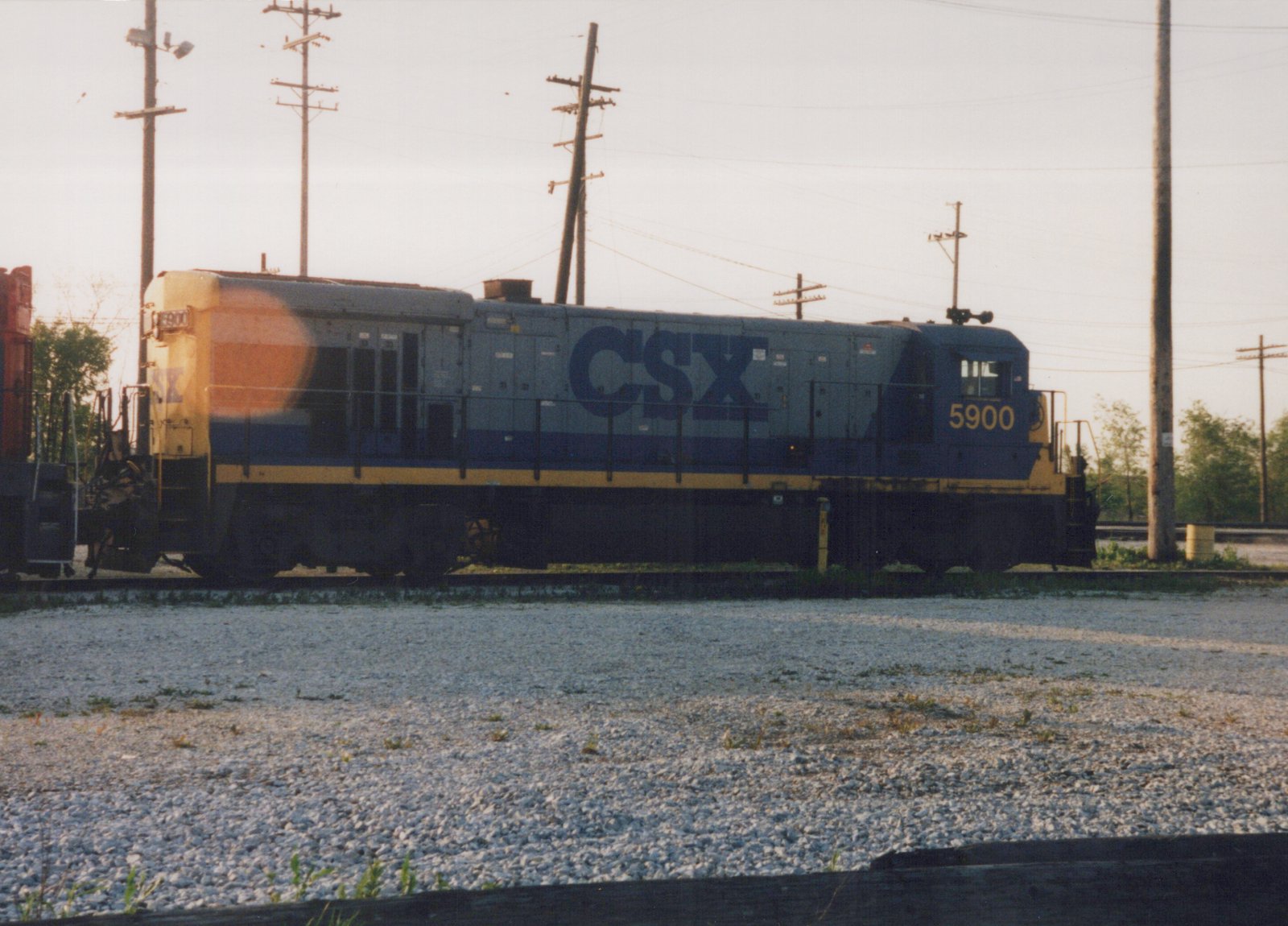 A side view of a blue and yellow CSX locomotive, number 5900, sitting on tracks surrounded by gravel under a clear sky.