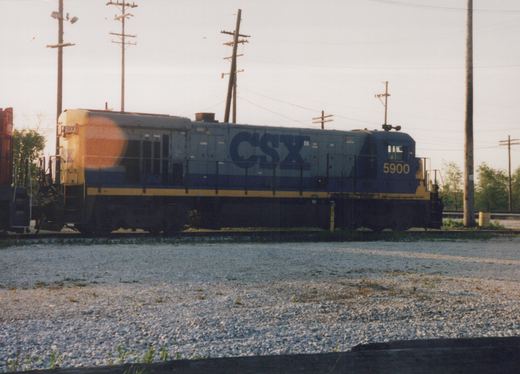 A side view of a blue and yellow CSX locomotive, number 5900, sitting on tracks surrounded by gravel under a clear sky.