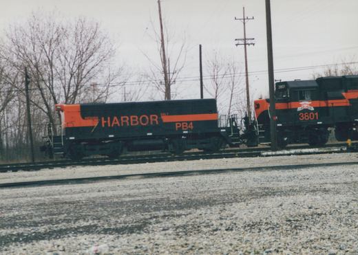 A black and orange Indiana Harbor Belt diesel locomotive, number 3801, is shown on tracks with bare trees in the background on an overcast winter day.