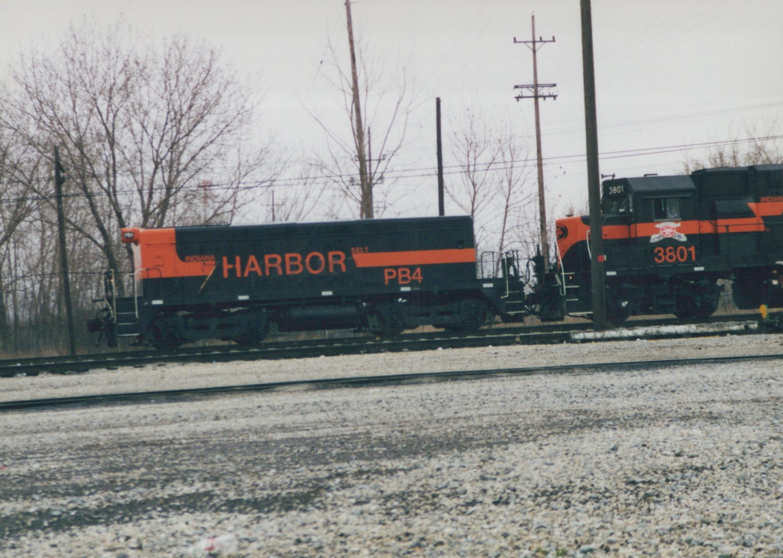 A black and orange Indiana Harbor Belt diesel locomotive, number 3801, is shown on tracks with bare trees in the background on an overcast winter day.
