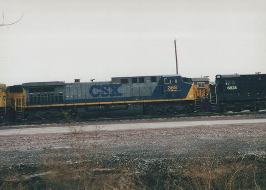 A blue and gray CSX diesel locomotive numbered 368 is parked on a track in a gravel yard. Other locomotives are visible behind it.