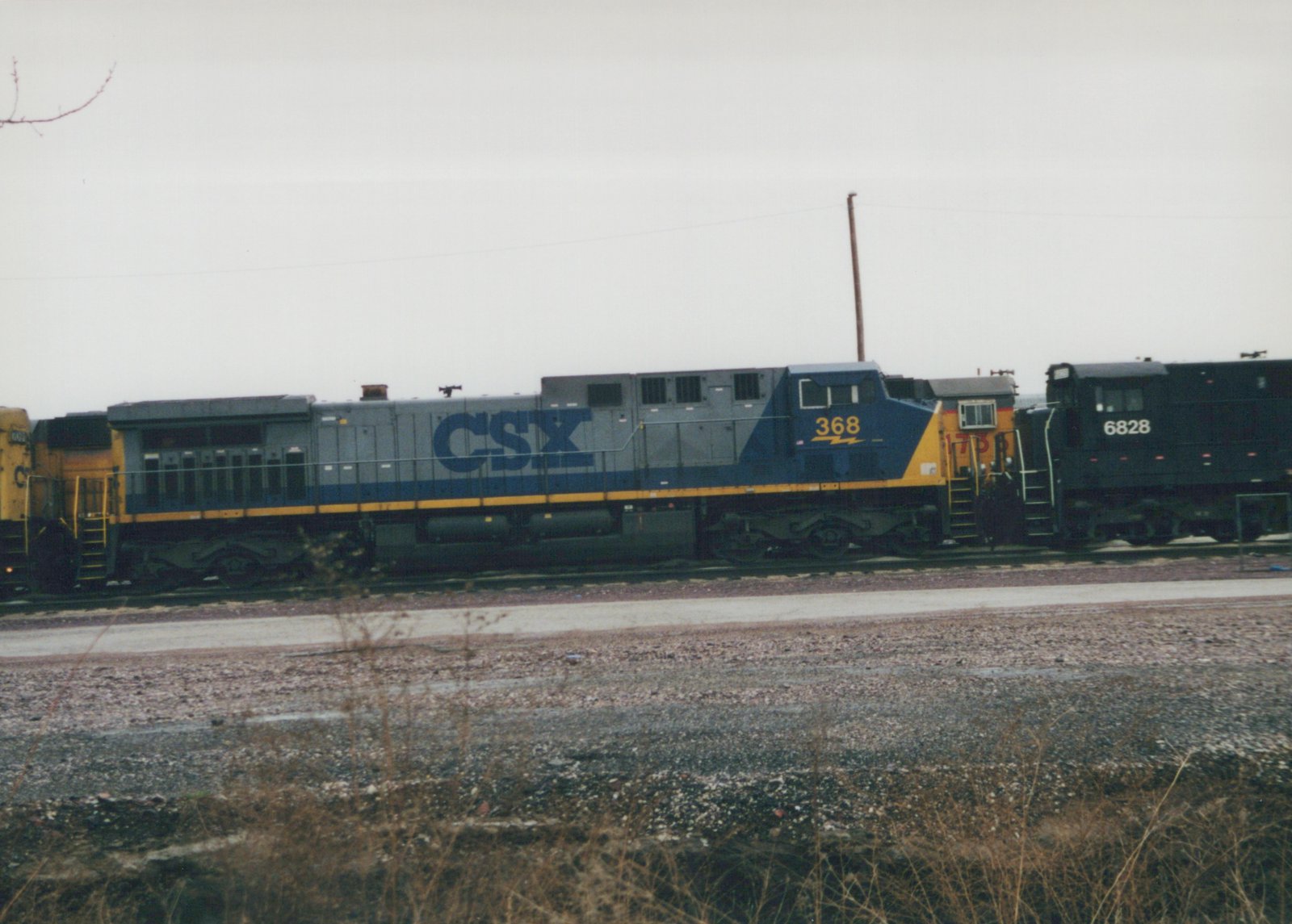 A blue and gray CSX diesel locomotive numbered 368 is parked on a track in a gravel yard. Other locomotives are visible behind it.