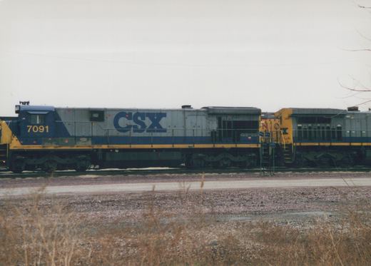 A side view of a CSX diesel locomotive, number 7091, painted in gray, blue, and yellow, coupled to another similar unit, number 368, on a set of railroad tracks.