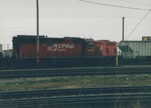 A red CP Rail System diesel locomotive numbered 4618 stands on multiple tracks in a rail yard next to a white freight car, under an overcast sky.