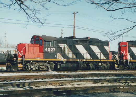 Two Canadian National diesel locomotives, numbered 4027 and 4034, are parked in a snowy railroad yard under a clear blue sky.