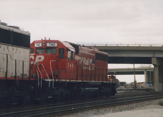 A red CP Rail System diesel locomotive numbered 740 is shown on tracks beneath a concrete bridge, with construction visible in the background.