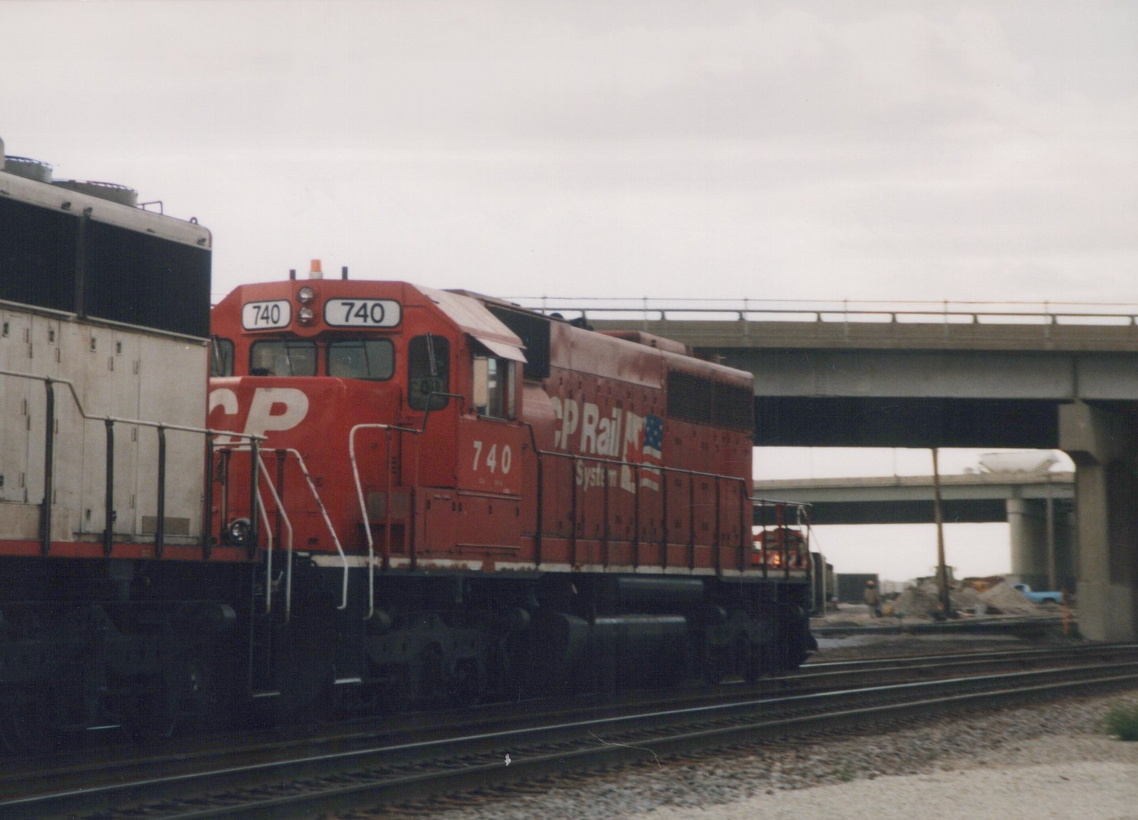 A red CP Rail System diesel locomotive numbered 740 is shown on tracks beneath a concrete bridge, with construction visible in the background.