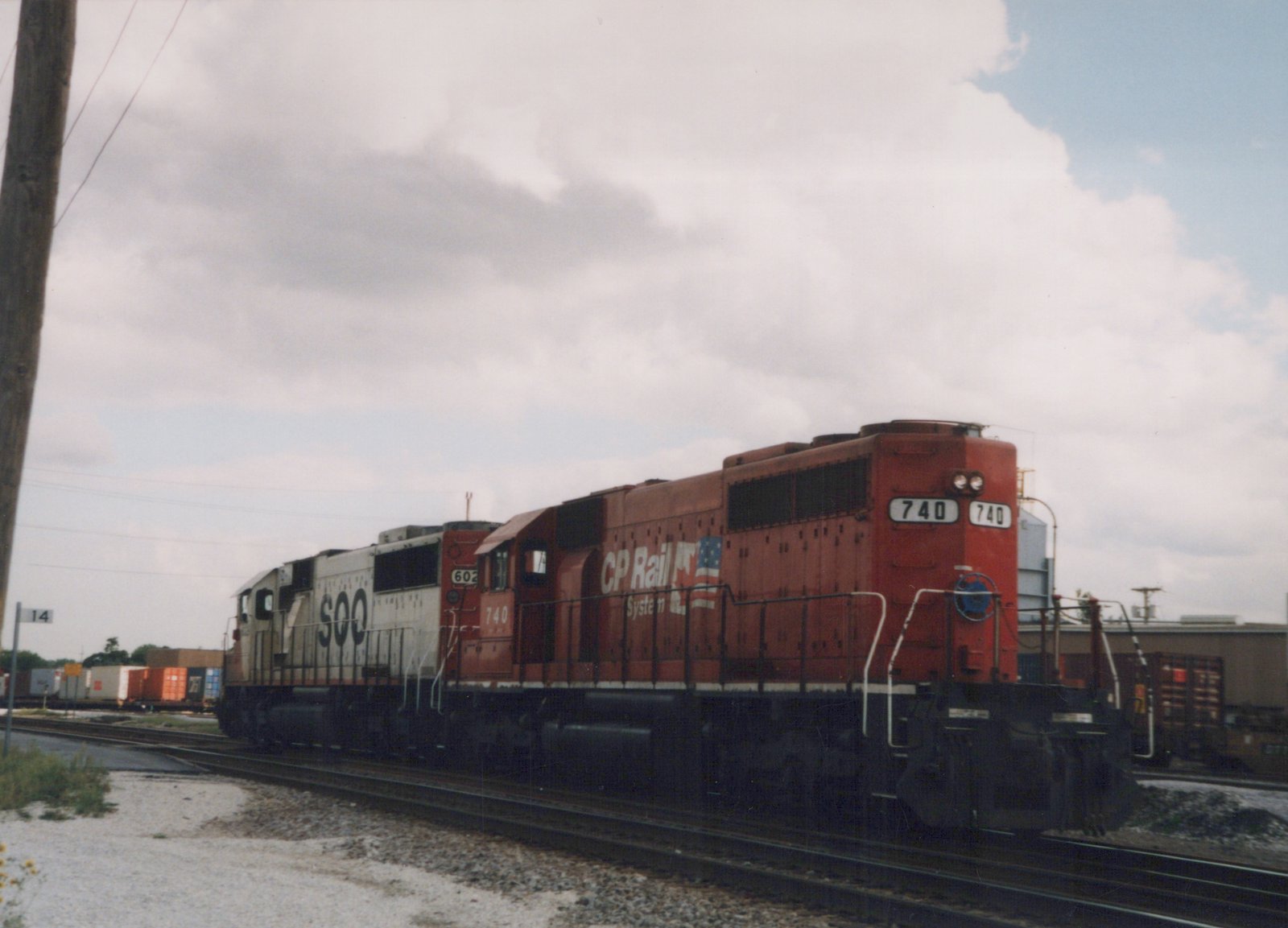 A red CP Rail System diesel locomotive numbered 740 is shown in a three-quarter front view, coupled with a white SOO Line locomotive numbered 602, on railroad tracks in a yard with overcast weather.