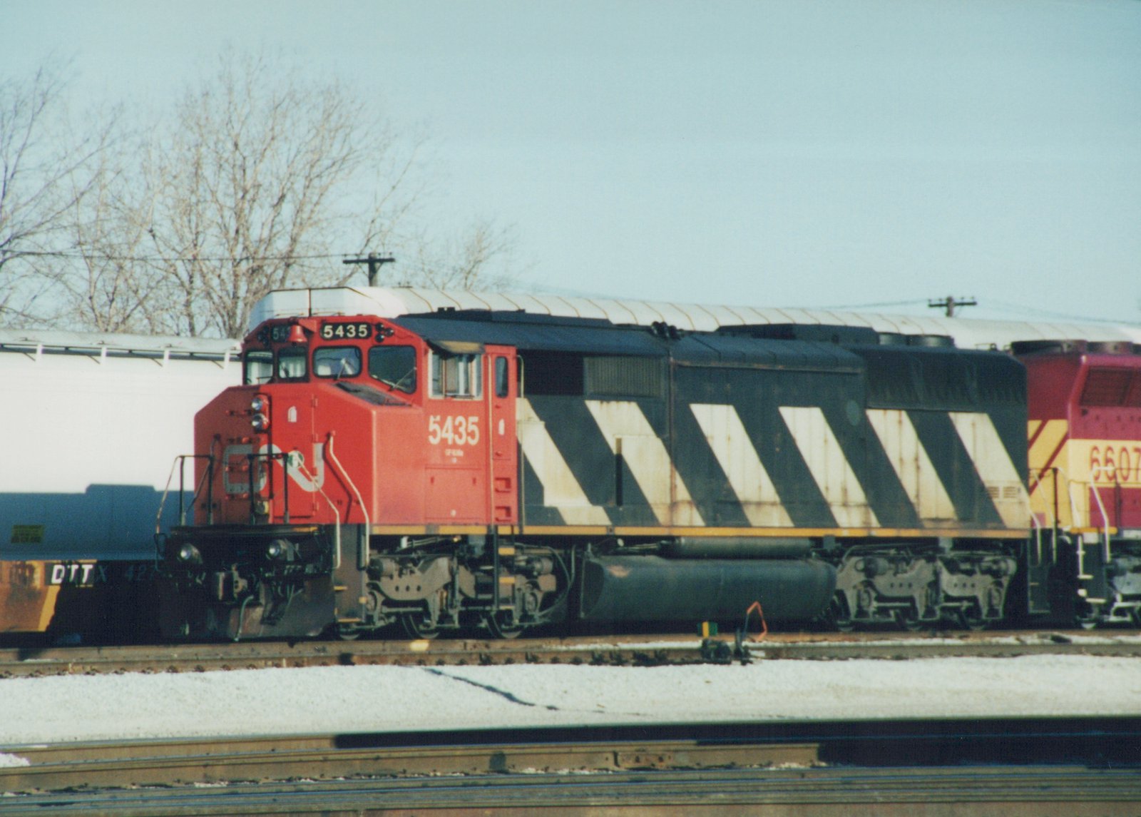 A side view of a red and black Canadian National diesel locomotive, number 5435, on a railroad track with snow on the ground, accompanied by another locomotive, number 6607, and a freight car in the background.