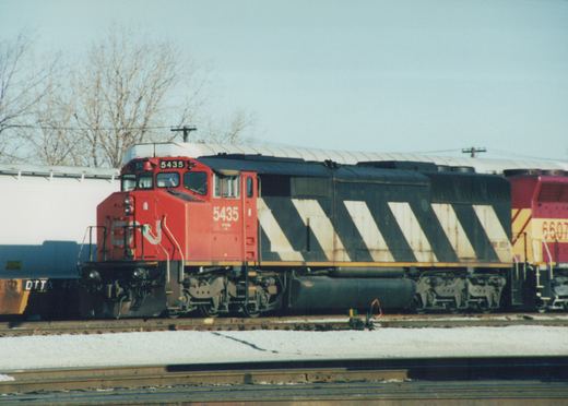 A side view of a red and black Canadian National diesel locomotive, number 5435, on a railroad track with snow on the ground, accompanied by another locomotive, number 6607, and a freight car in the background.