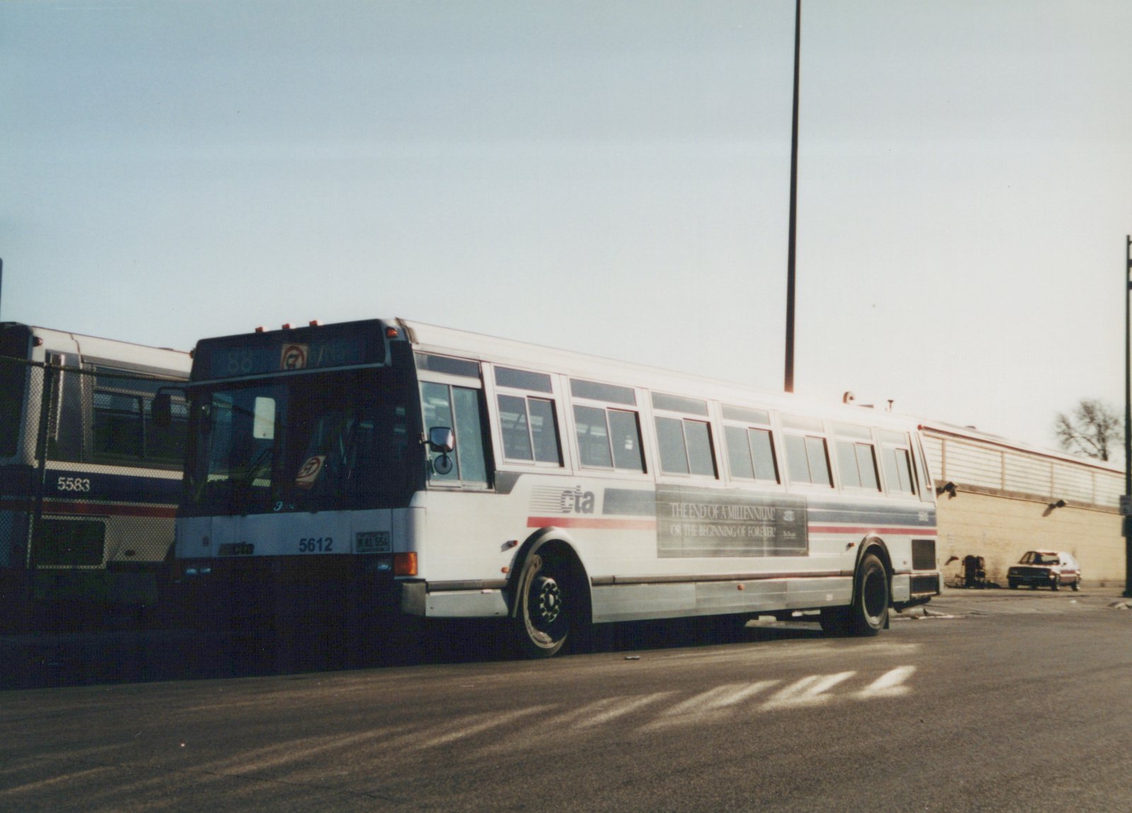 Side view of a white Chicago Transit Authority bus numbered 5612, parked on a street with a clear sky and a brick building in the background.