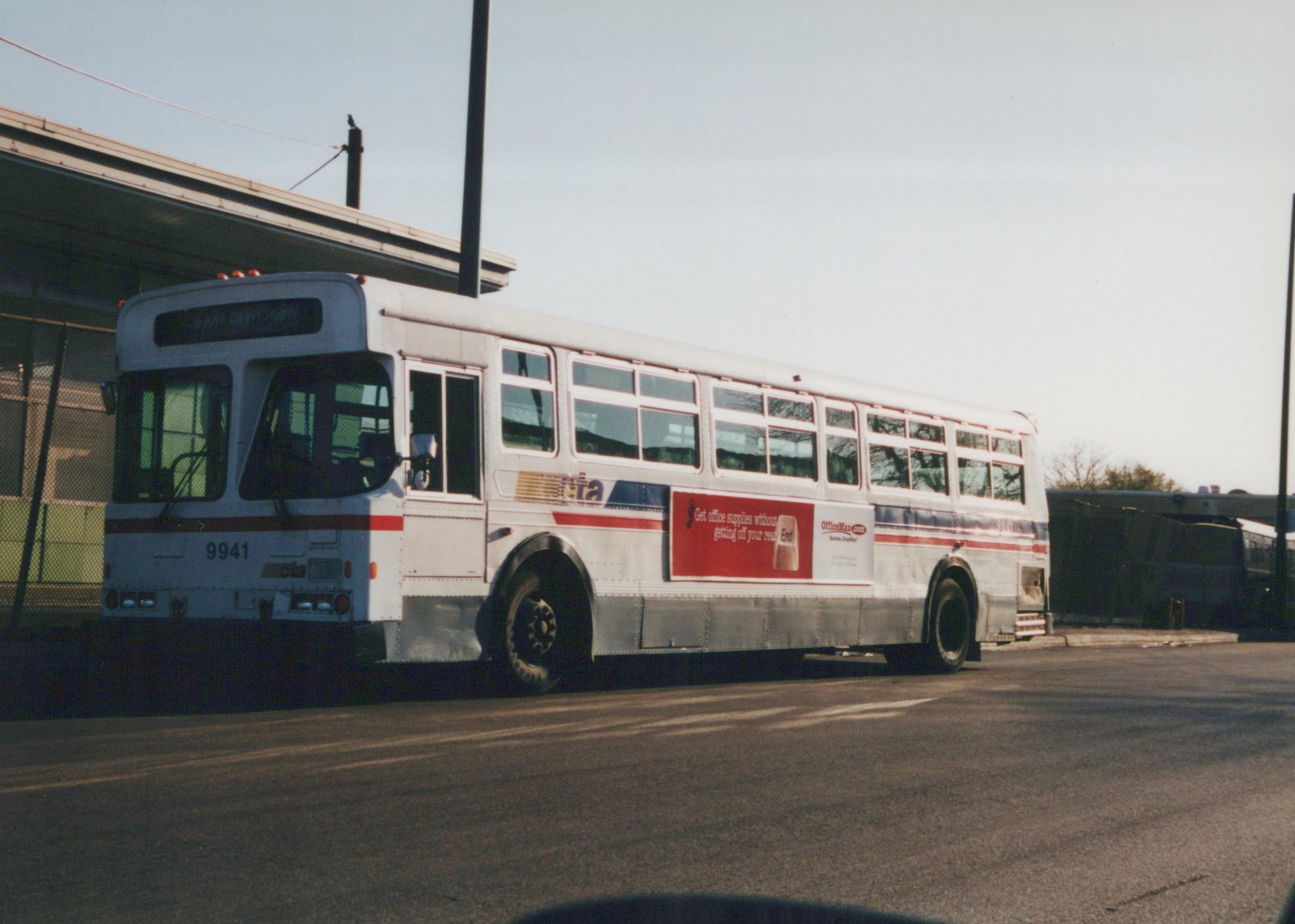 A white Chicago Transit Authority bus with red and blue stripes, number 9941, is parked on a street with an OfficeMax ad on its side and a destination sign reading '5401 OLYMPIC BOULEVARD'.