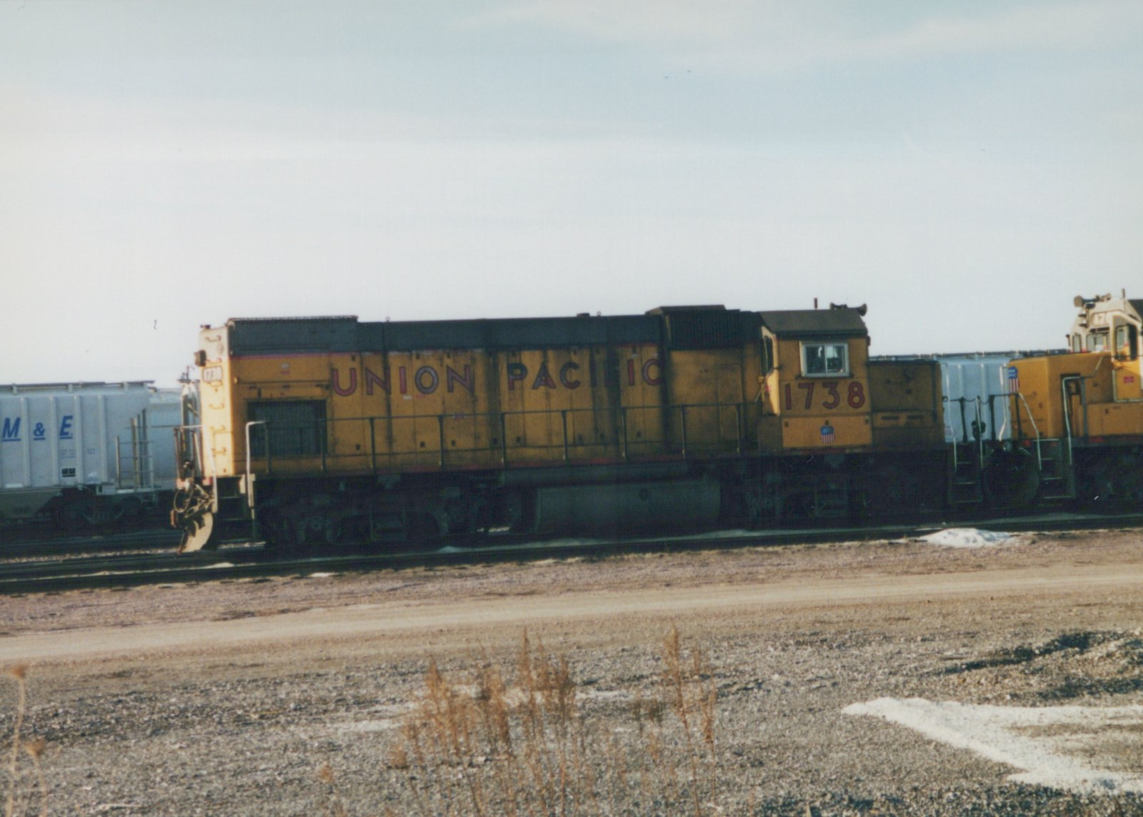 A side view of a yellow Union Pacific locomotive, number 1738, parked on railroad tracks in a gravel yard with patches of snow on the ground.