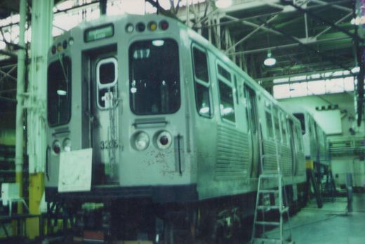 A silver CTA 2000-series rapid transit car, numbered 4117, is shown from a three-quarter front view inside a spacious carbarn, with another car, 3206, visible behind it.
