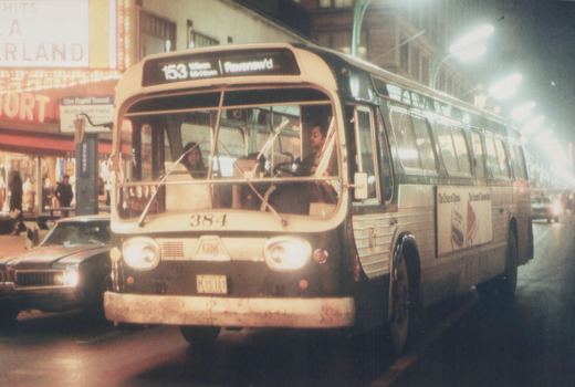 A Chicago Transit Authority New Look bus, number 384, is shown on route 153 at night, traveling down a street past storefronts and a parked car.