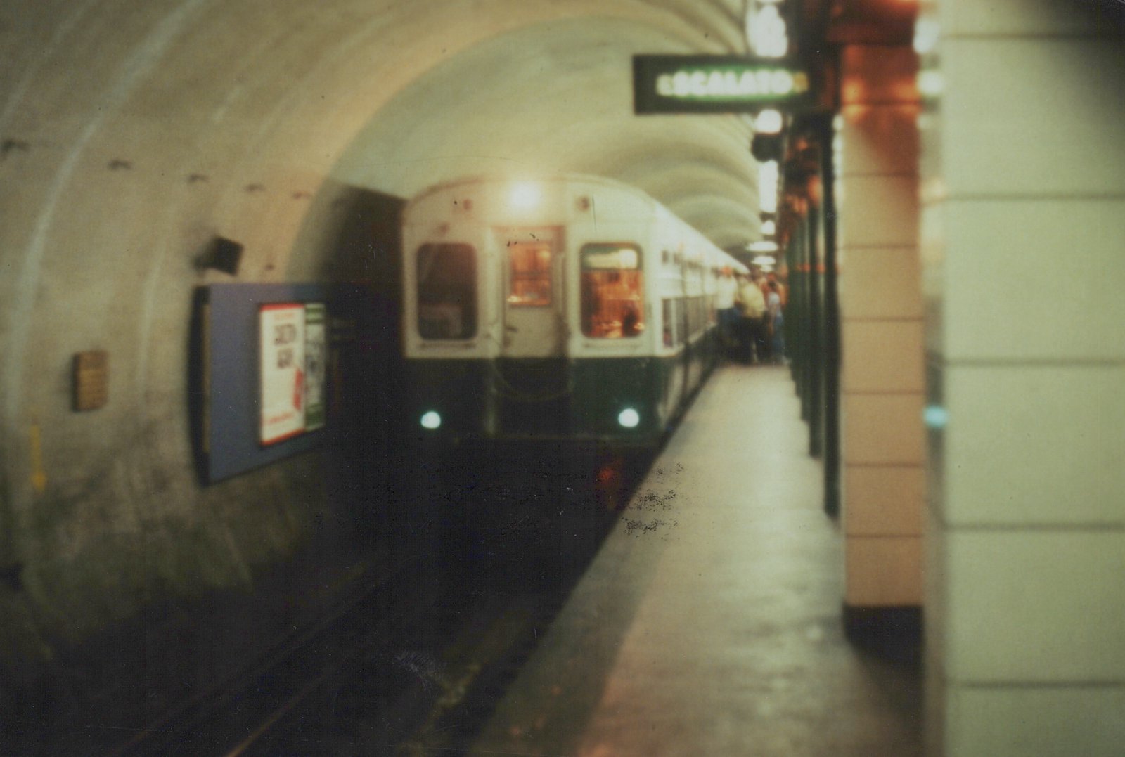 A white and green CTA 'L' train is stopped at a station platform in a curved subway tunnel with an overhead 'ESCALATOR' sign.