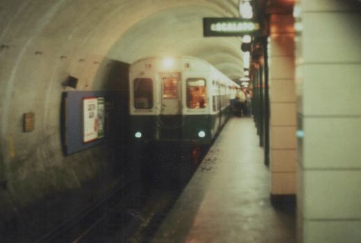 A white and green CTA 'L' train is stopped at a station platform in a curved subway tunnel with an overhead 'ESCALATOR' sign.