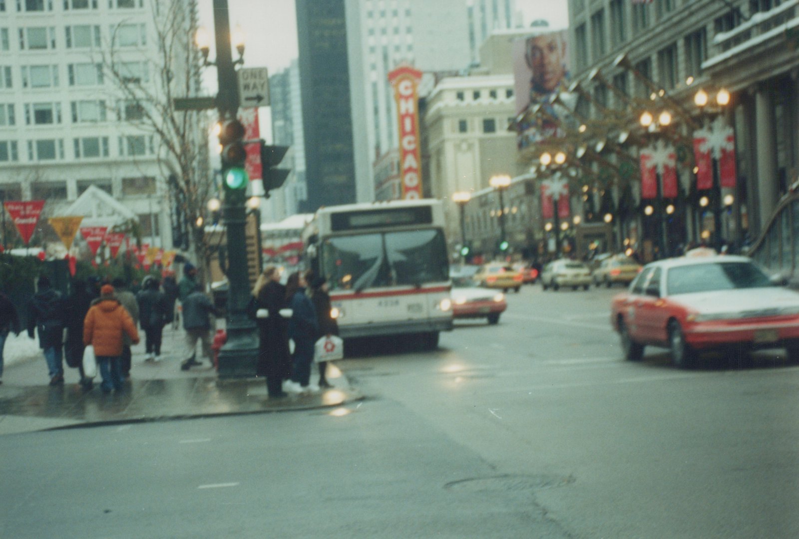 A white and red CTA bus with the number 4228 on its front, stopped on a wet city street lined with buildings and decorated for the holidays, with pedestrians on the sidewalk and cars in traffic.