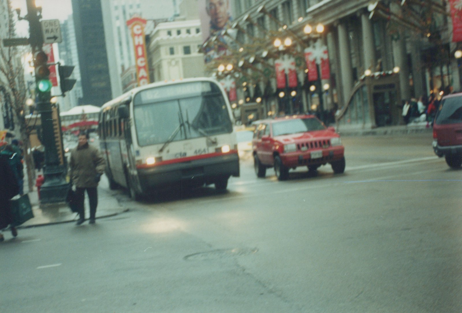 A white and red CTA bus, number 4641, drives on a city street with pedestrians and other vehicles nearby, with holiday lights and a 'CHICAGO' sign on a building in the background.