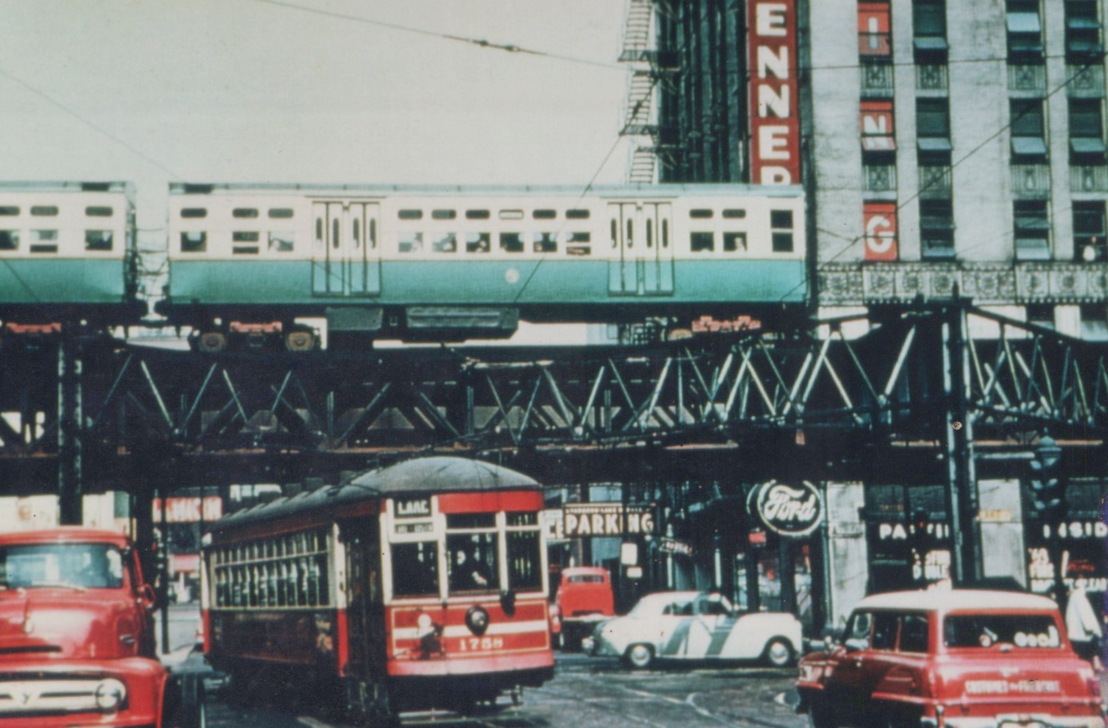 A red and cream streetcar marked 'LAKE' and numbered 1758 runs on a city street beneath an elevated green and cream rapid transit train, surrounded by 1940s automobiles and storefront signs including 'ENNEPER' and 'Ford'.