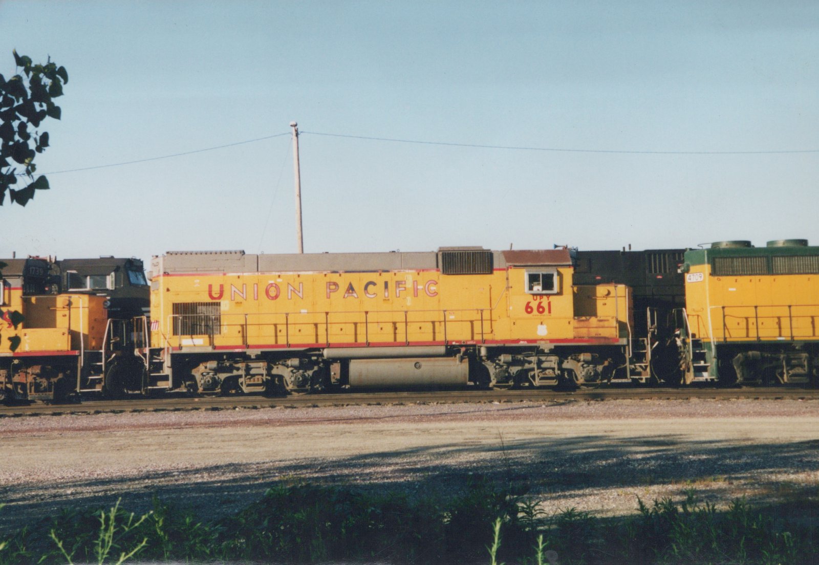 Three yellow Union Pacific diesel locomotives, numbers 661, 1739, and 4709, are coupled together on a railroad track in a gravel yard, with a clear blue sky overhead.