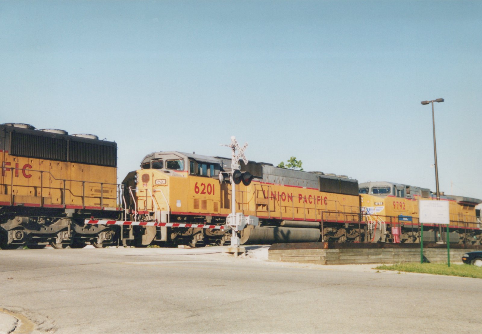 Two yellow Union Pacific diesel locomotives, numbered 6201 and 9792, are stopped at a grade crossing on a sunny day.
