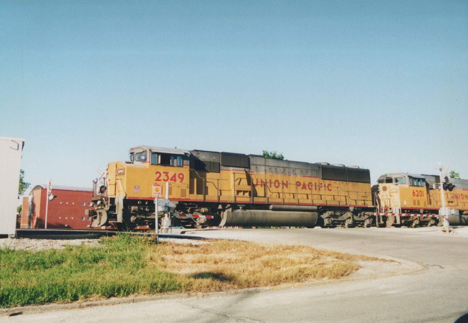 Two yellow Union Pacific locomotives stopped at a railroad crossing with a clear blue sky and some greenery in the foreground.