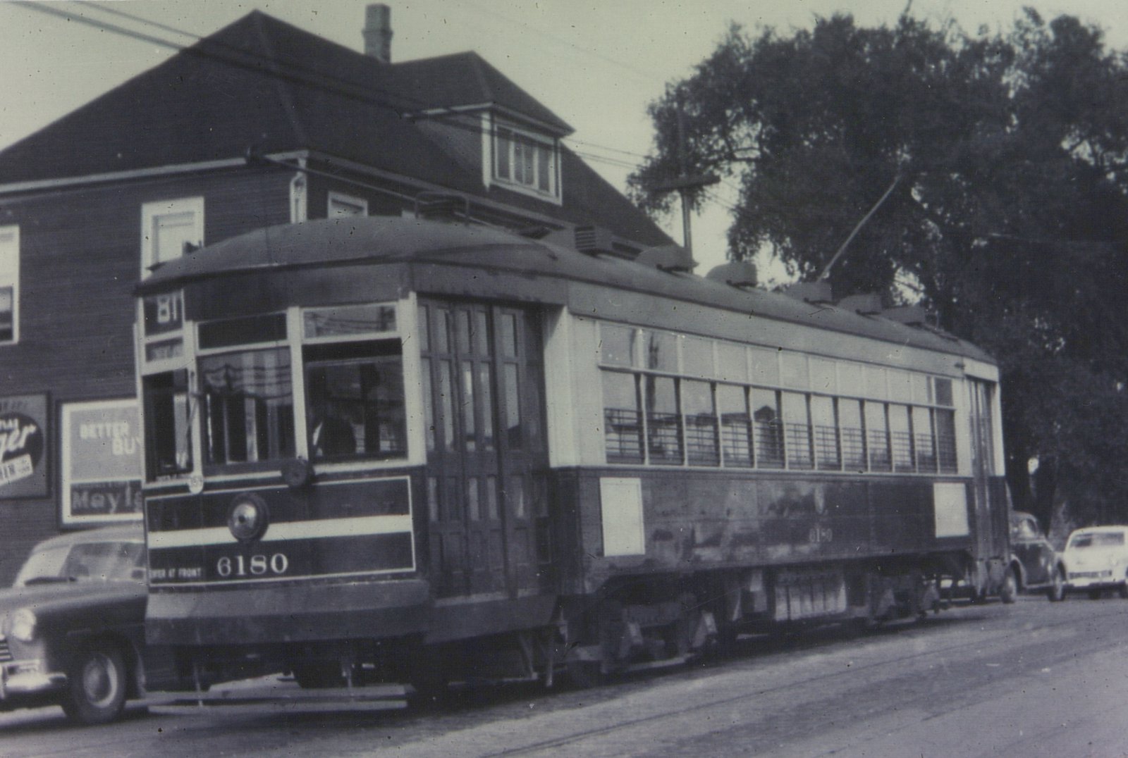 A black and white photograph of a vintage Chicago Surface Lines streetcar numbered 6180, showing its side and front with a trolley pole raised, parked on a street with cars and a building in the background.