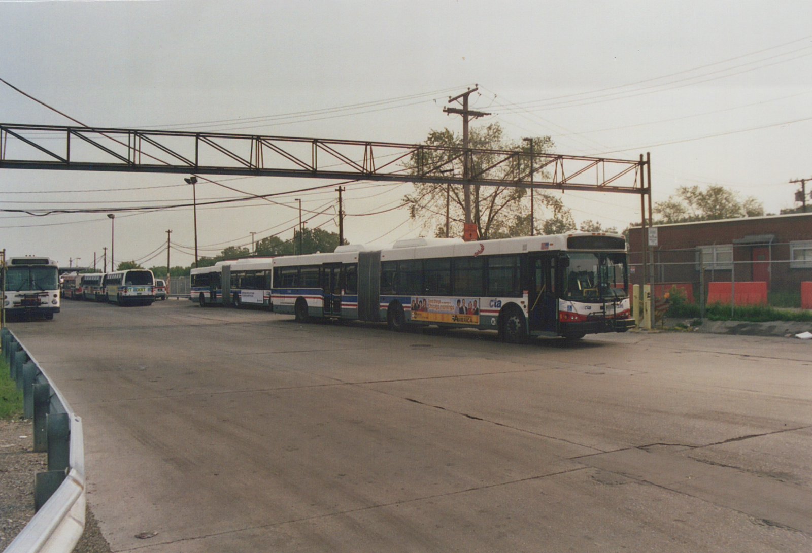 A line of CTA buses, including an articulated bus numbered 7596, parked in a yard with an elevated structure overhead and a chain-link fence in the background.