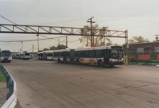 A line of CTA buses, including an articulated bus numbered 7596, parked in a yard with an elevated structure overhead and a chain-link fence in the background.