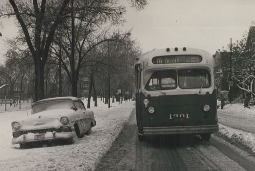 Front view of a vintage Chicago Transit Authority bus on a snowy street, with a 1950s car parked to the side and bare trees in the background.