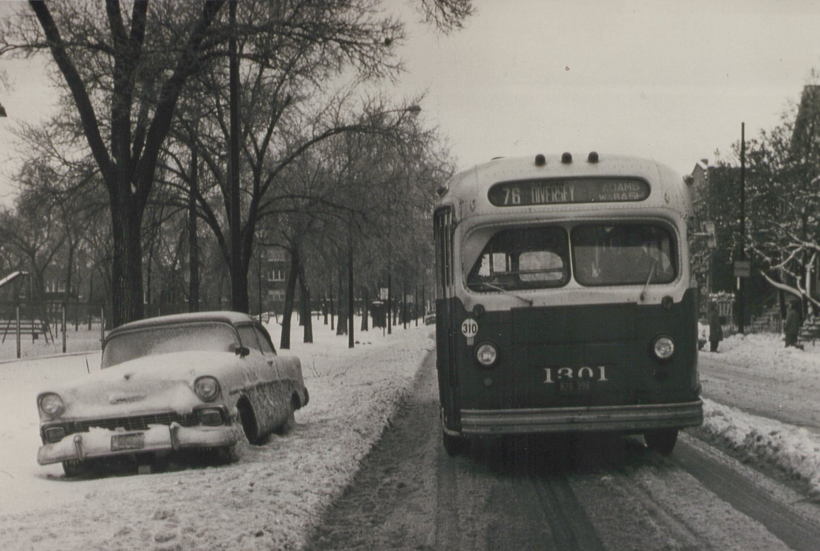 Front view of a vintage Chicago Transit Authority bus on a snowy street, with a 1950s car parked to the side and bare trees in the background.