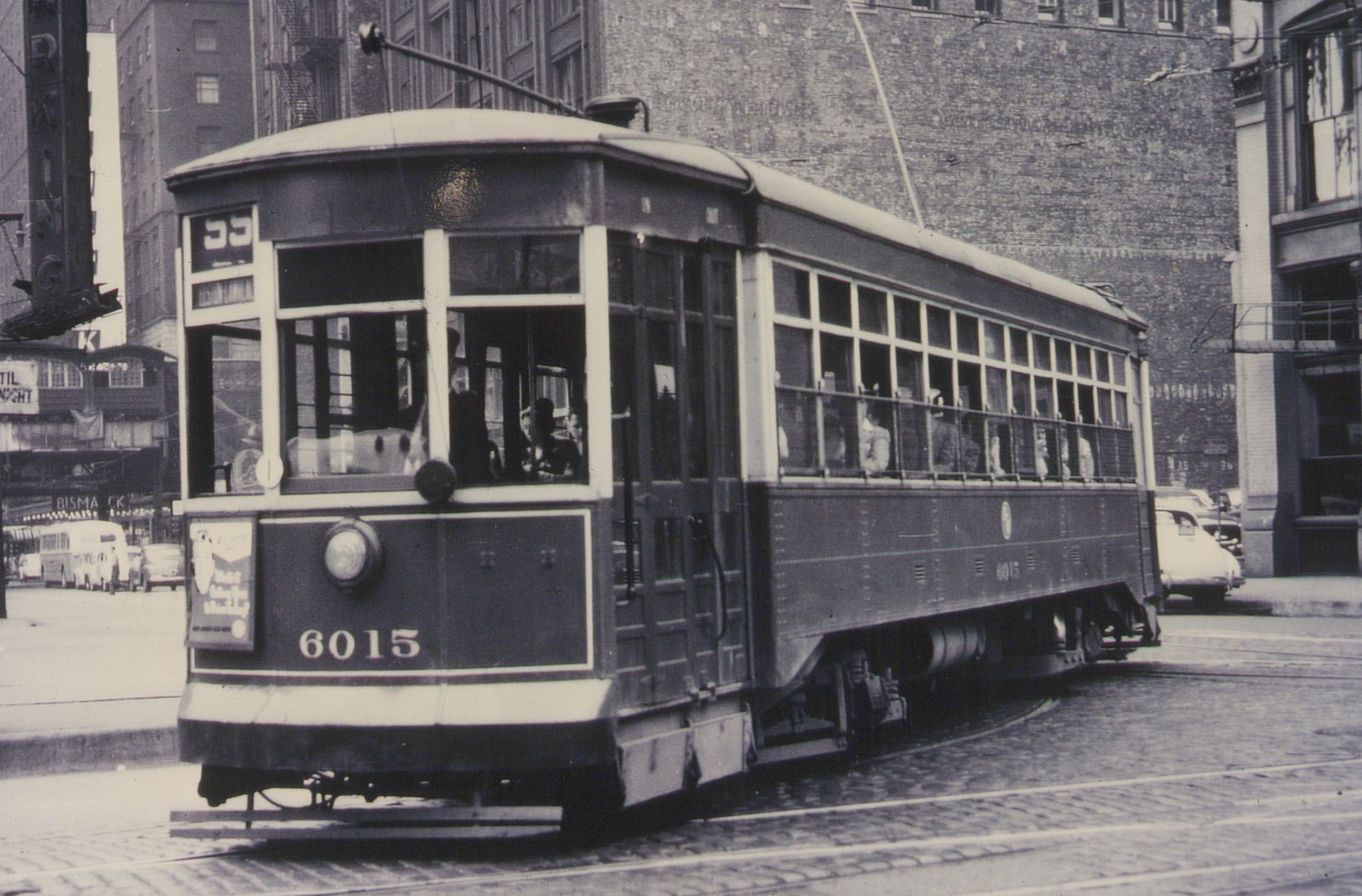 A vintage Chicago streetcar, number 6015, is shown on a city street with passengers visible inside and a trolley pole connecting to overhead wires.