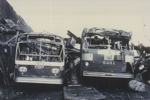 Two burned-out CTA buses, one numbered 3153 and the other 5481, are shown front-on in a wrecked state on a street with debris around them.