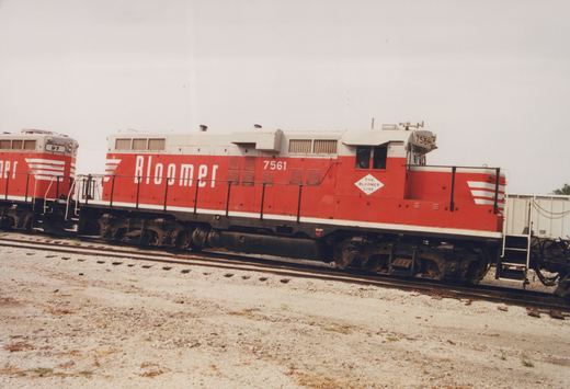 Side view of two red and white Bloomer Line diesel locomotives, 7561 and 91, parked on parallel tracks in a gravel yard under an overcast sky.